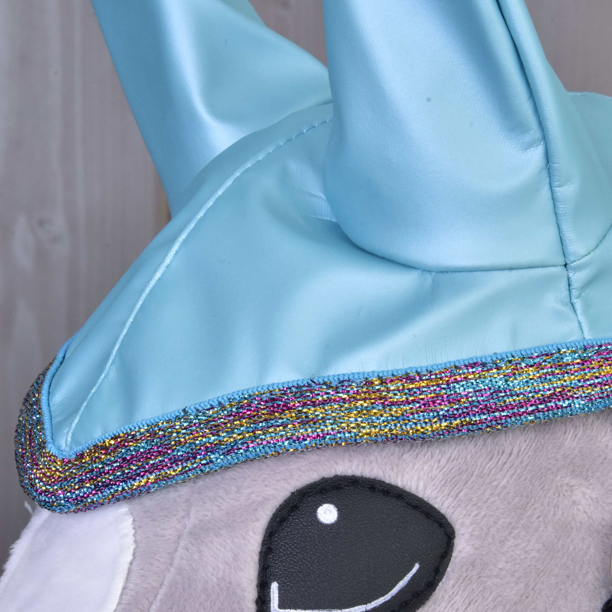 Close-up of the pink, gold and blue glitter edging below the glossy ears of the Hobby Horse Raincoat Light Blue