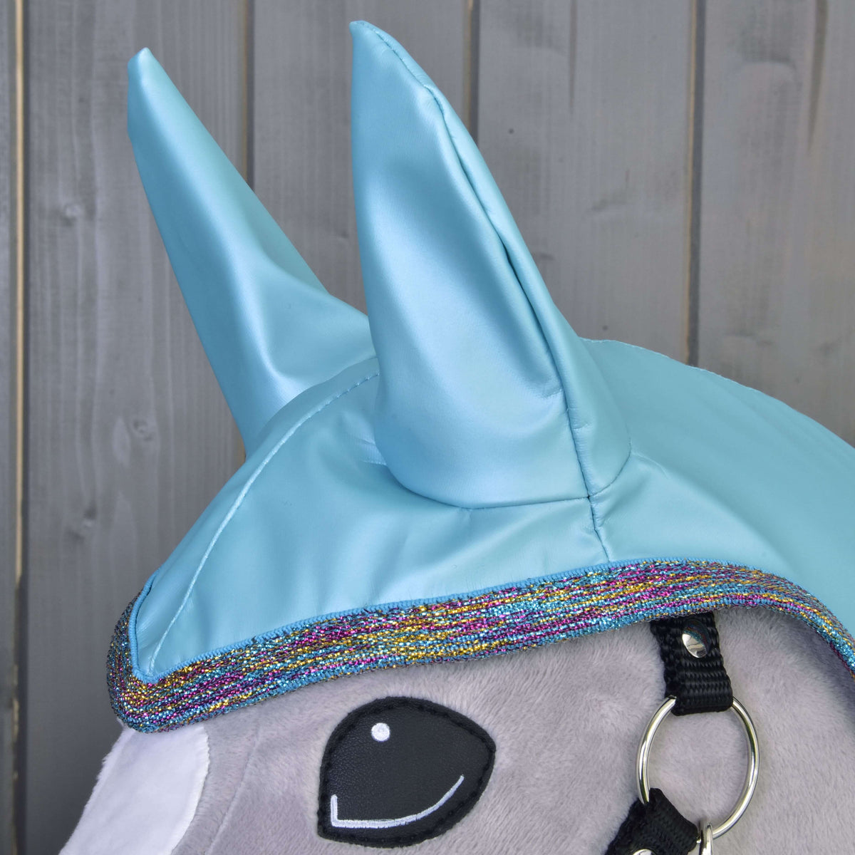 Glossy light blue raincoat ears and glitter edging on a grey Hobby Horse, with the black halter strap and silver ring beside