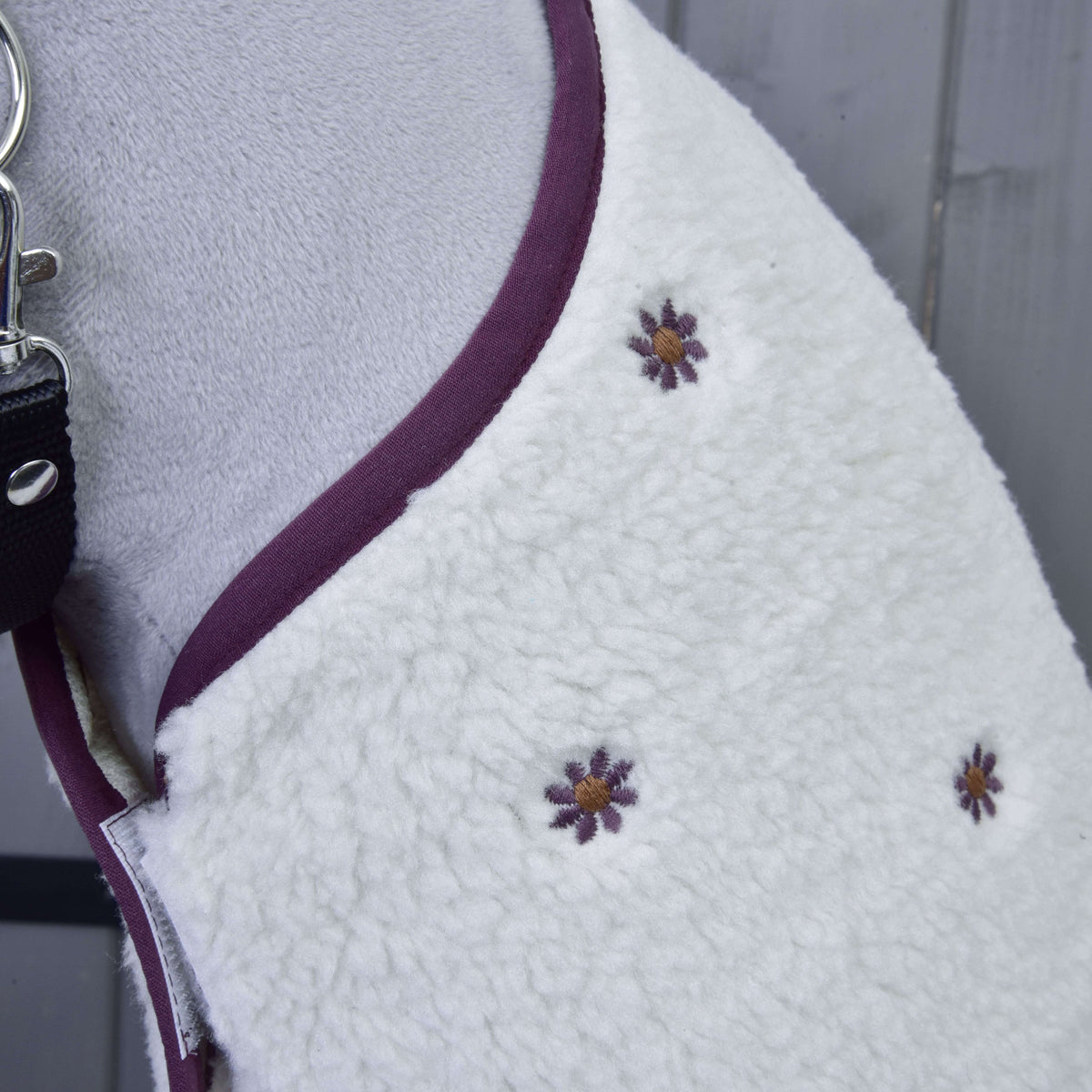 Detail of the small embroidered plum flowers with golden centres on the cream sherpa blanket at the neck