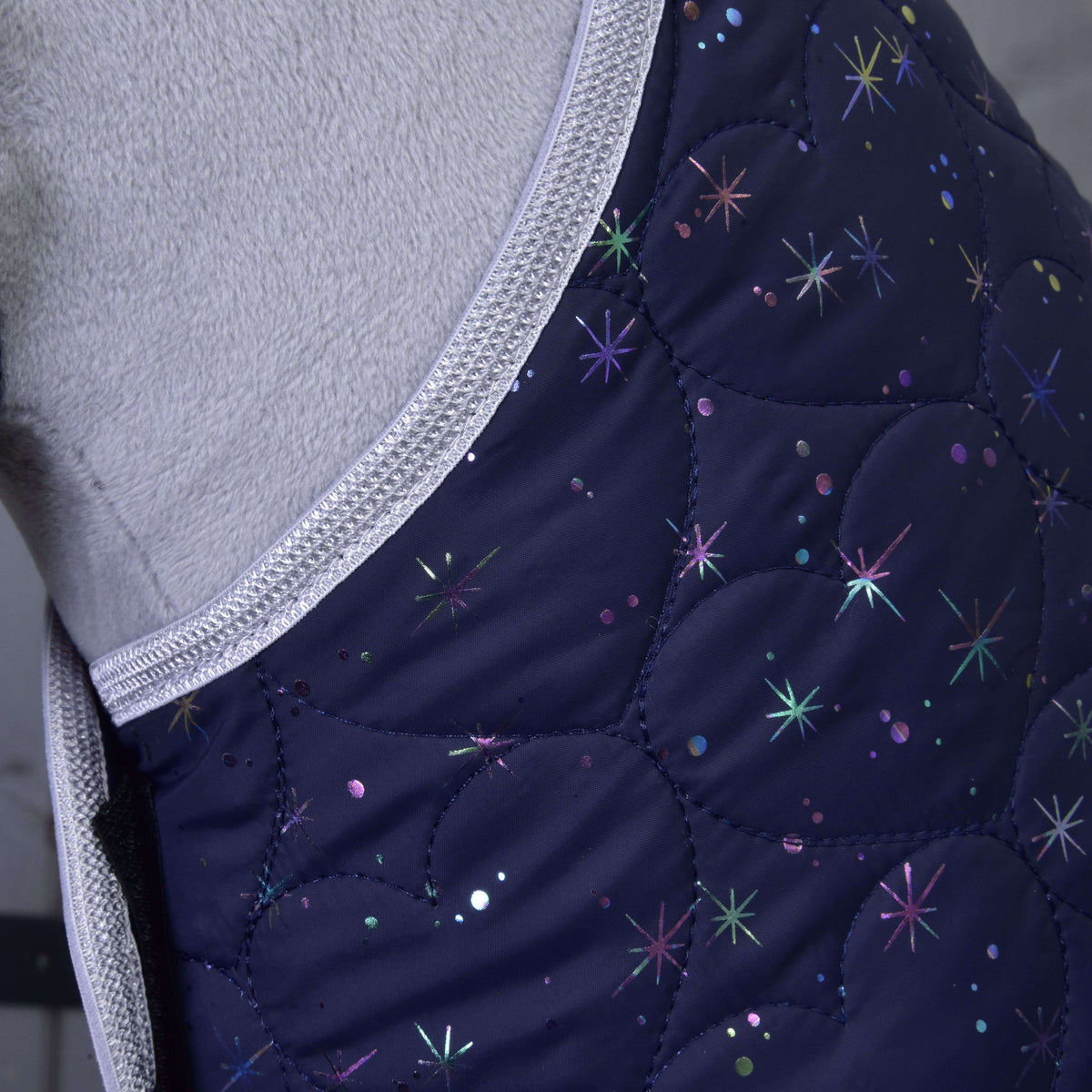 Detail of the heart-shaped quilting and holographic stars on the navy blanket against a grey plush neck