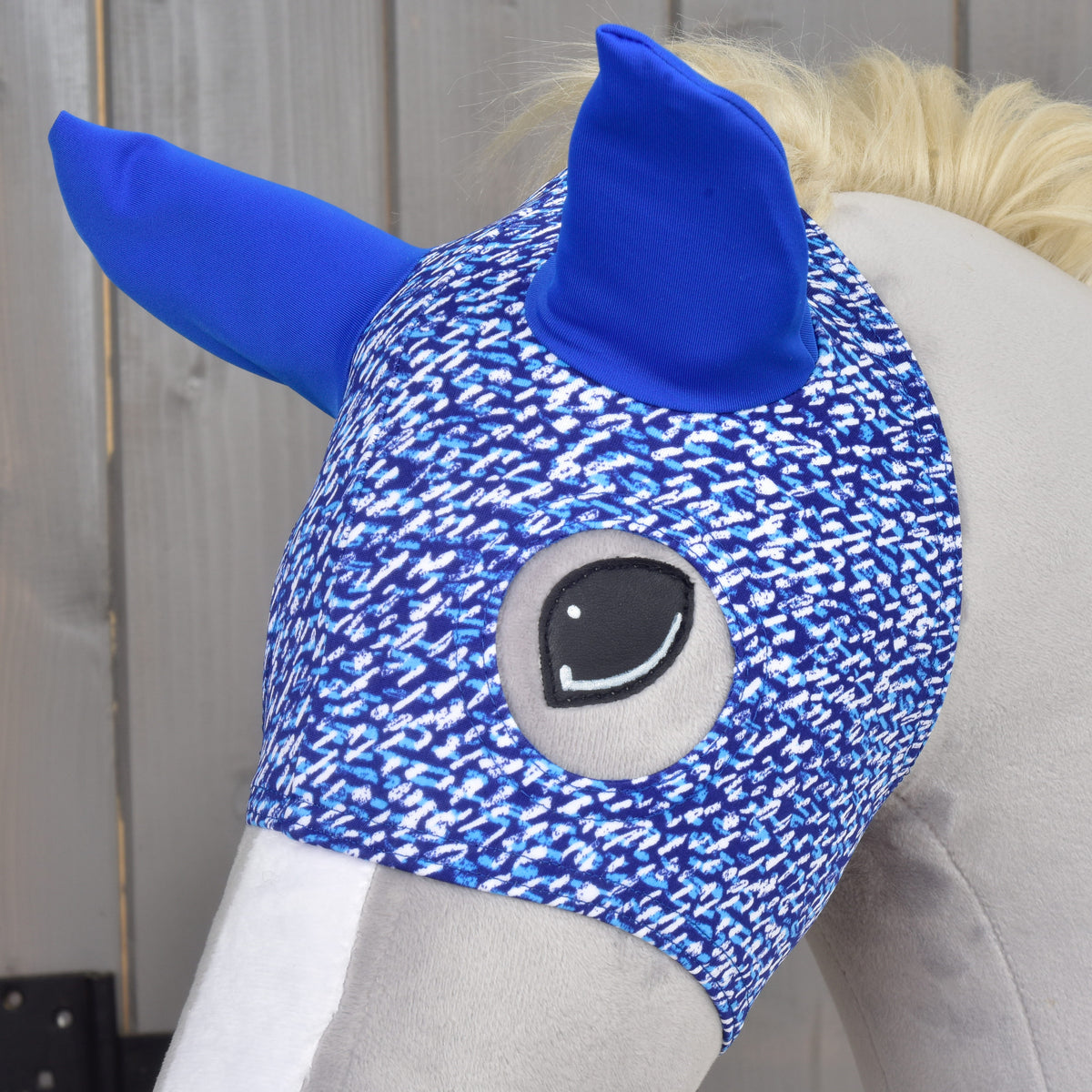 Närbild av Mask See på en grå käpphäst, med det broderade ögat inramat av det spräckliga blå tyget