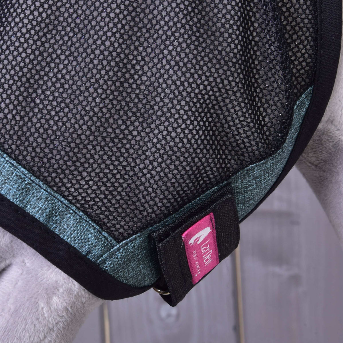 Close-up of the cheek strap with pink LarDen label and metal ring on the Hobby Horse Fly Mask De Luxe Turquoise