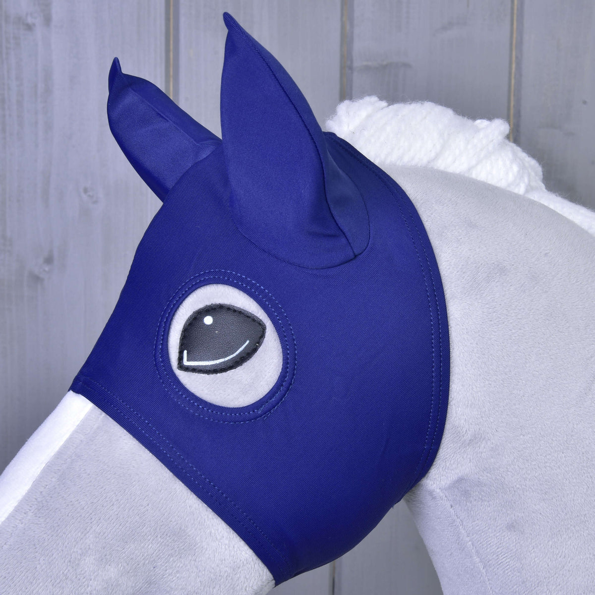 Närbild av masken med öronskydd i marinblått tyg på en grå käpphäst, det svarta ögat inramat av öppningen