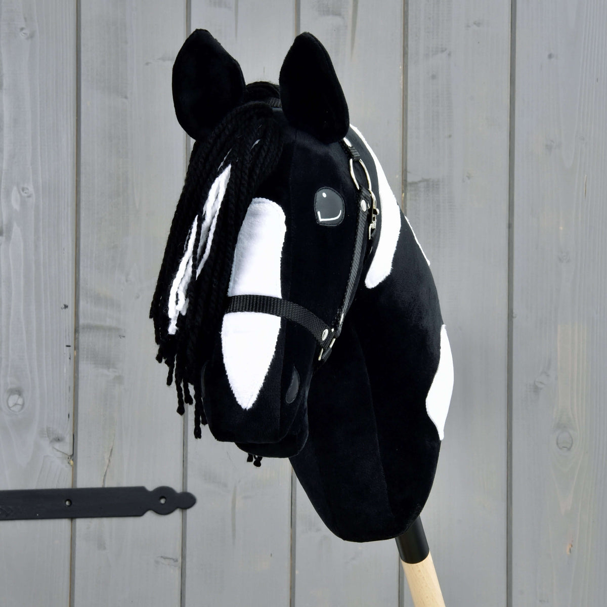 Hobby Horse Merlin med svart grimma framifrån, svart pannlugg av garn med vita slingor över en bred vit bläs