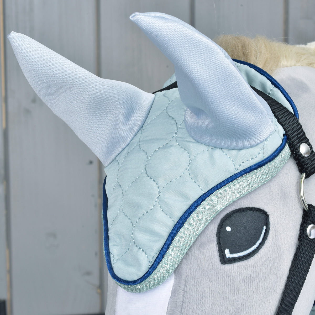 Närbild av flughuvan i Set Mint på en grå käpphäst: ljusblå quiltning och öron, marinblå passpoal och glitterkant