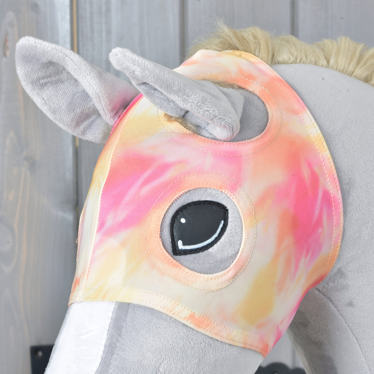Närbild av masken Mirage på en grå käpphäst, med plyschöronen som sticker ut och sydda kanter runt ögonöppningen