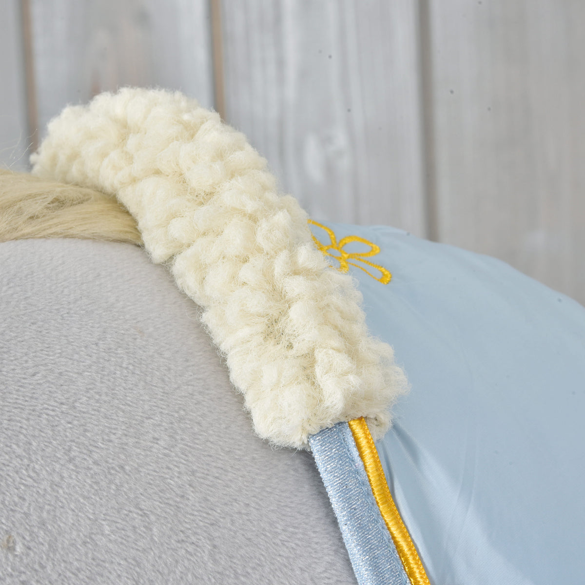 Close-up of the cream curly fleece collar, yellow piping and blue glitter trim of the Stable Blanket Misty on a grey Hobby Horse