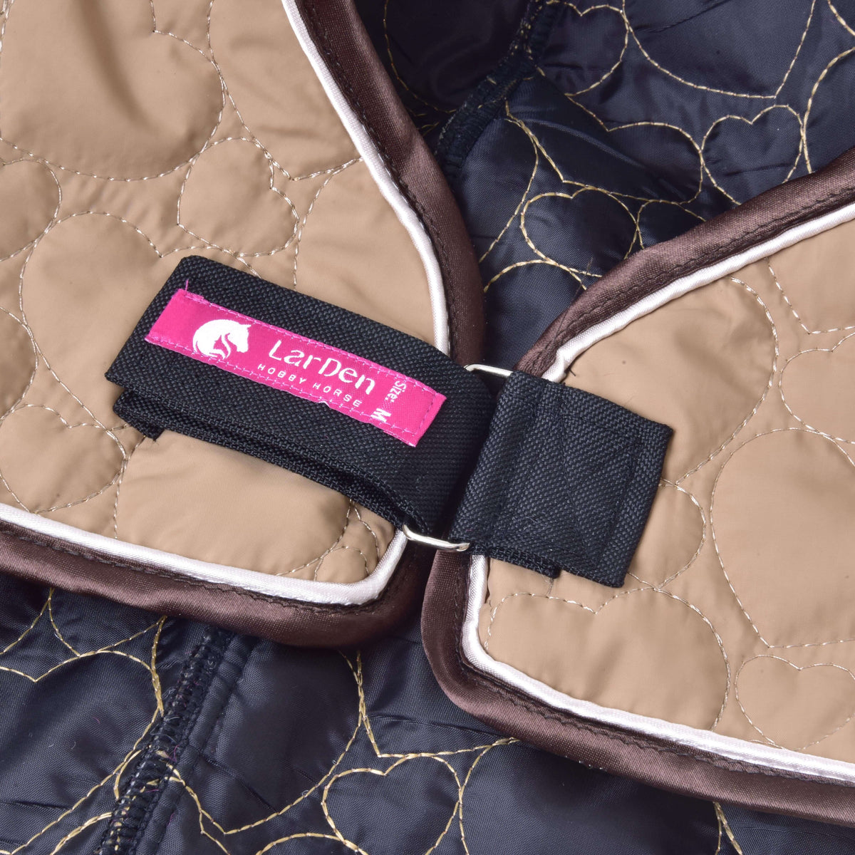 Close-up of the black Velcro strap with pink LarDen label and metal ring on the beige heart-quilted Hobby Horse neck cover