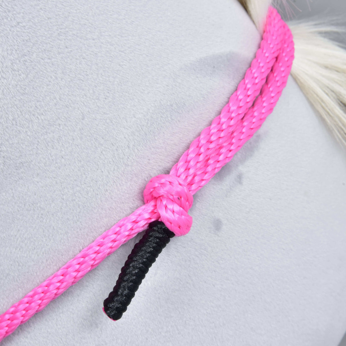Närbild av det rosa flätade repet på halsringen Pink Festive med en knut och svartlindad ände mot en grå plyschhals