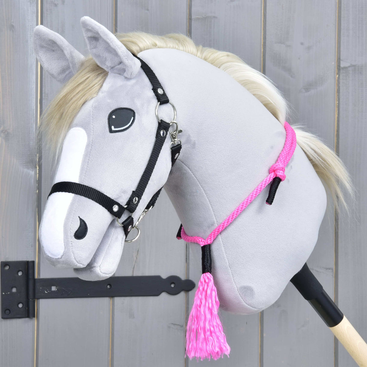 Grå käpphäst med krämvit man och svart grimma med halsringen Pink Festive runt halsen, med den rosa tofsen