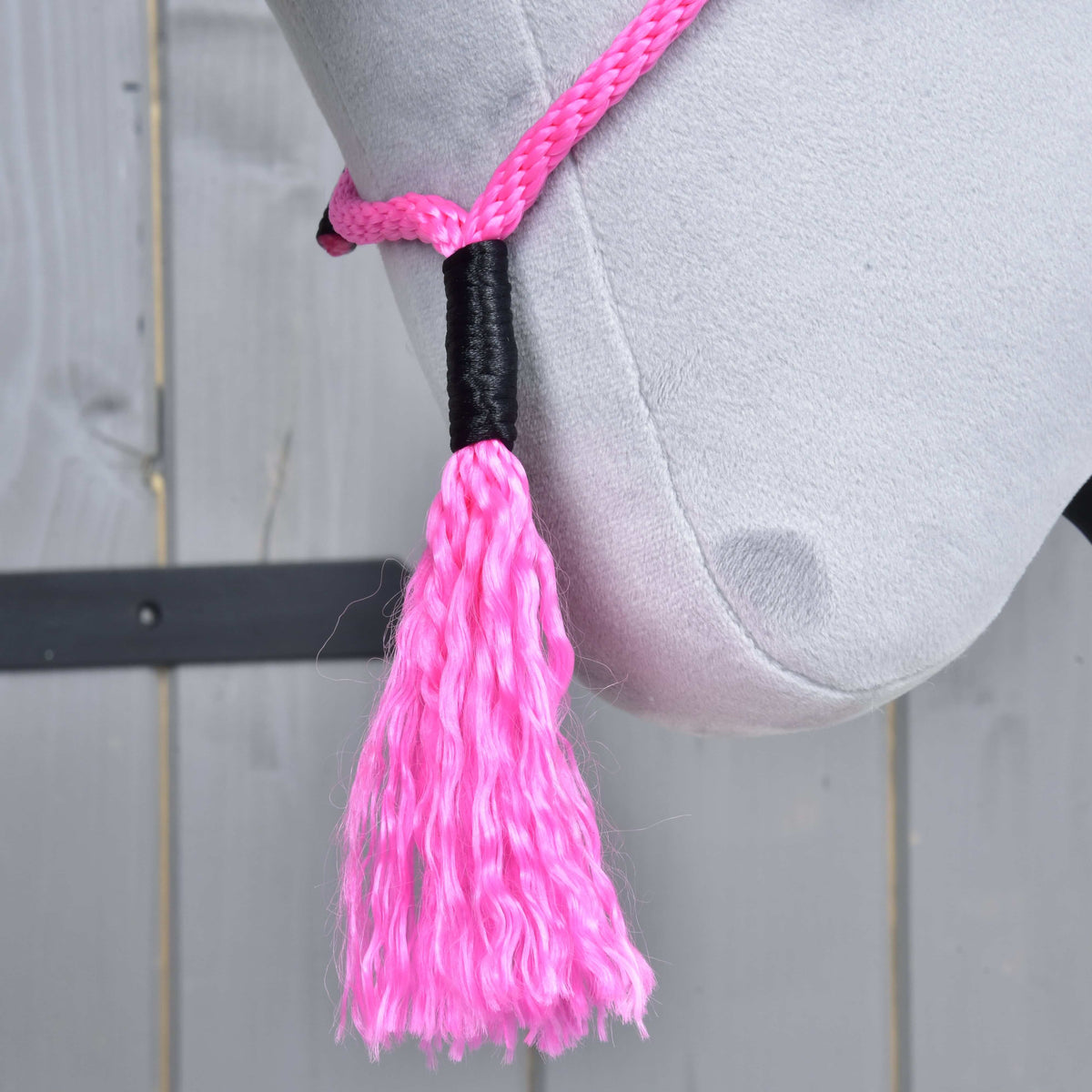 Den rosa tofsen på halsringen Pink Festive med svartlindad topp, hängande under käken på en grå käpphäst