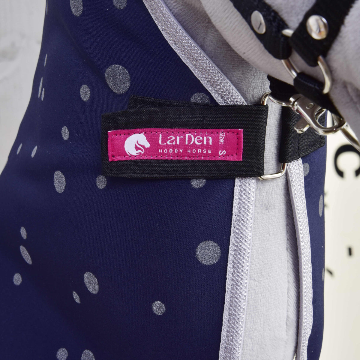 Close-up of the pink LarDen Hobby Horse label on the black chest strap of the navy dotted stable blanket
