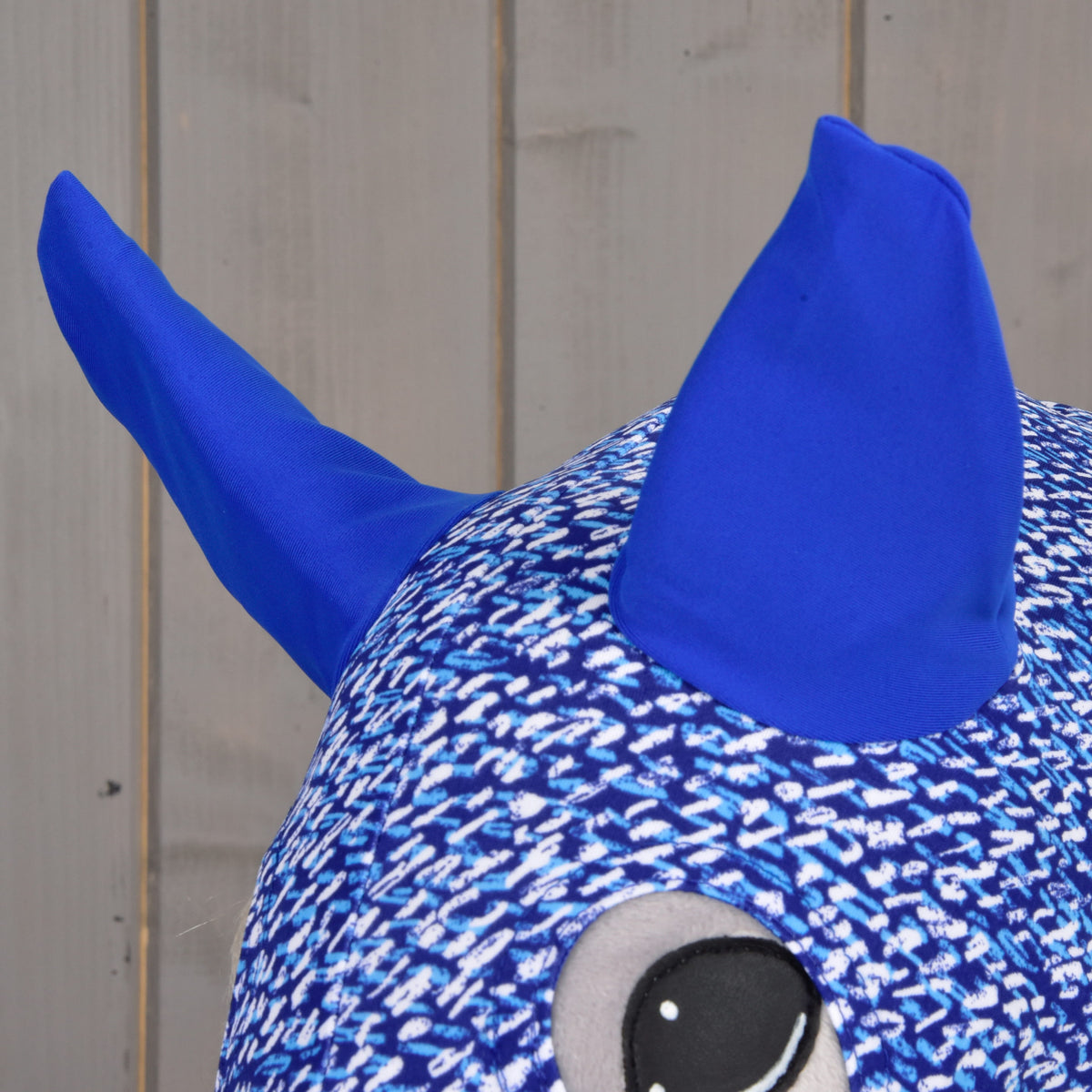 Close-up of the bright royal blue ears and the eye opening of the patterned suit on a grey Hobby Horse