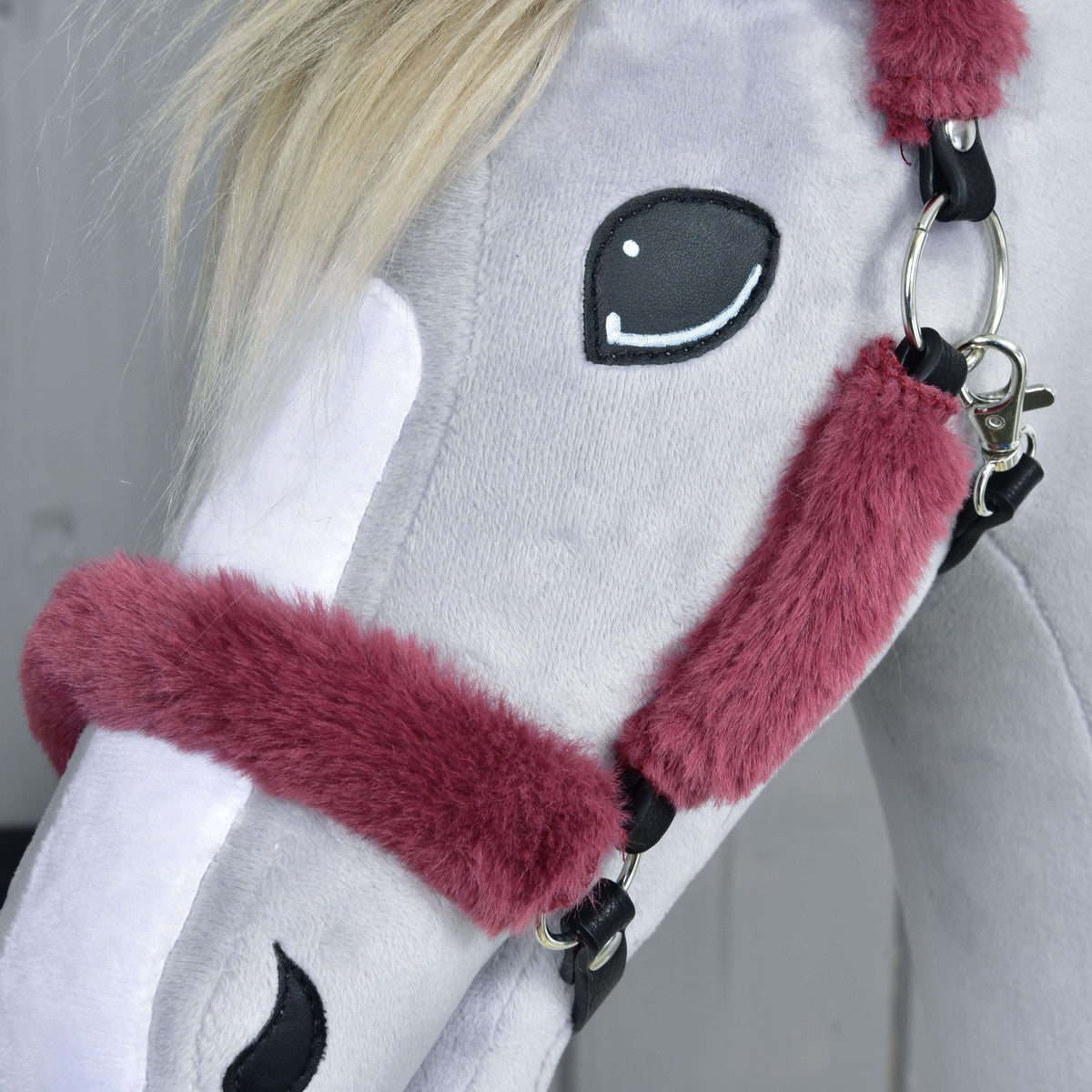 Close-up of the maroon fur noseband and cheekpiece beside the stitched eye, with a silver ring and snap hook
