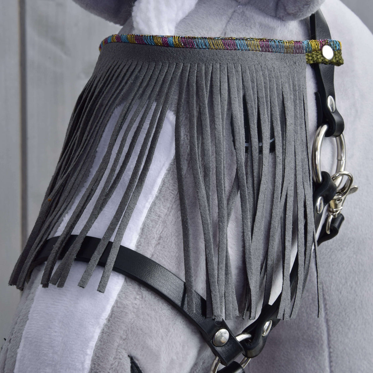 Close-up of the grey fringes hanging over the eye of a grey Hobby Horse, with black halter straps below