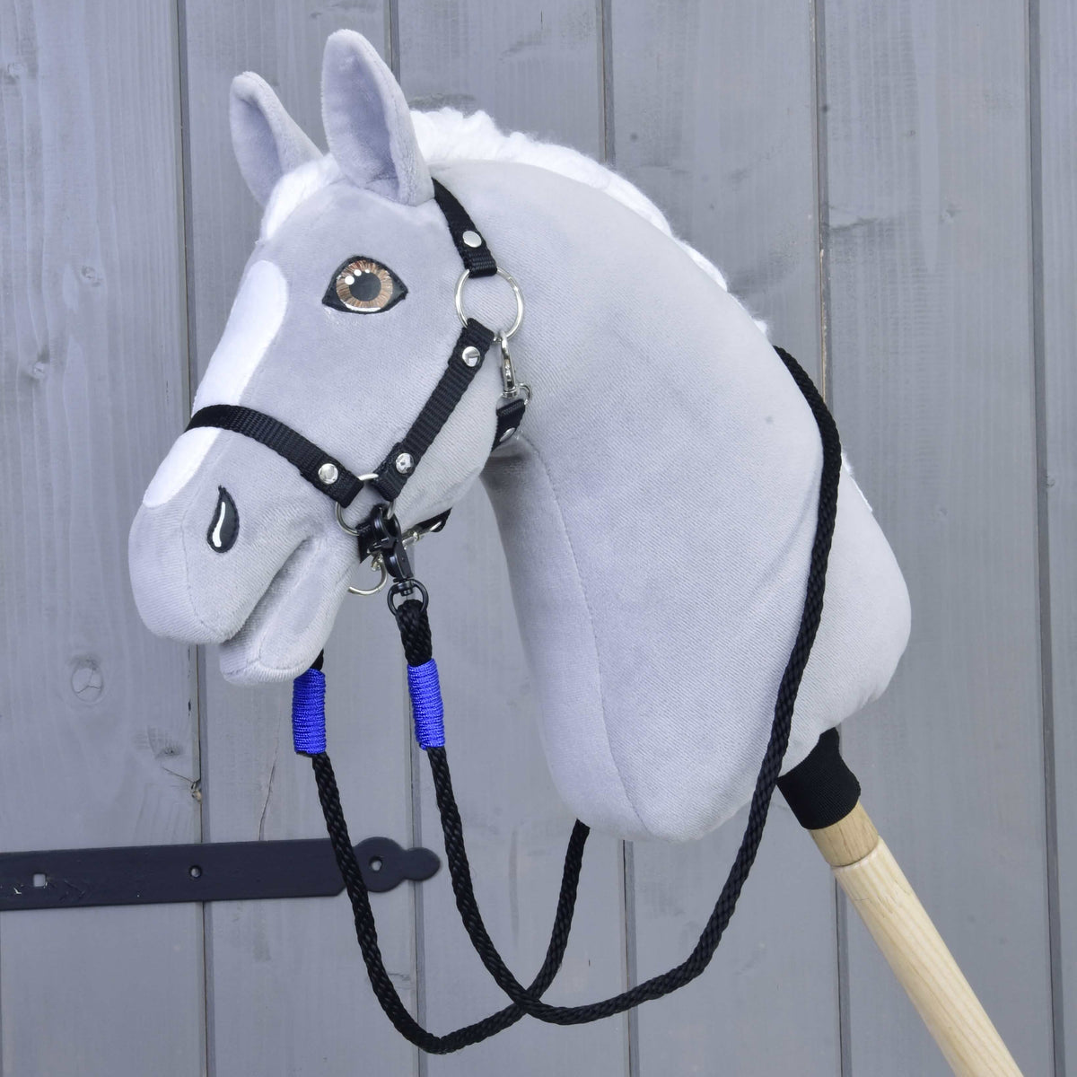 Grey plush Hobby Horse with a black halter and the black rope reins with blue wraps clipped under its chin