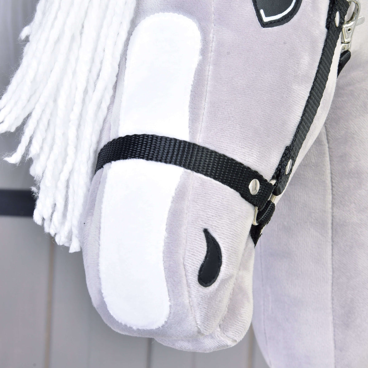 Close-up of the white blaze, black stitched nostril and black halter noseband on the light grey plush muzzle