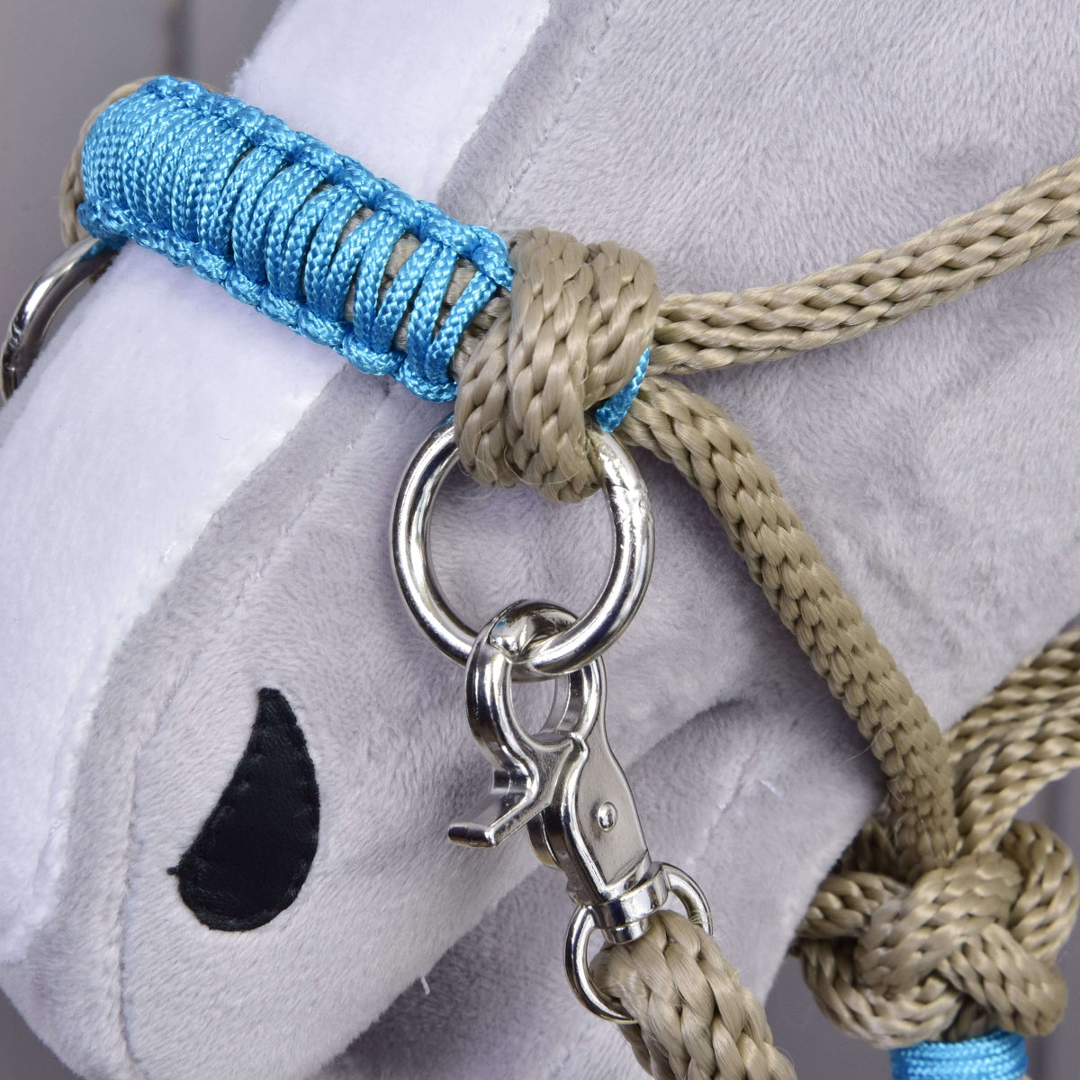 Makrodetalj av den blå flätningen på nosremmen på Hobby Horse repset Nature Blue bredvid en beige knut och silverfärgad ring