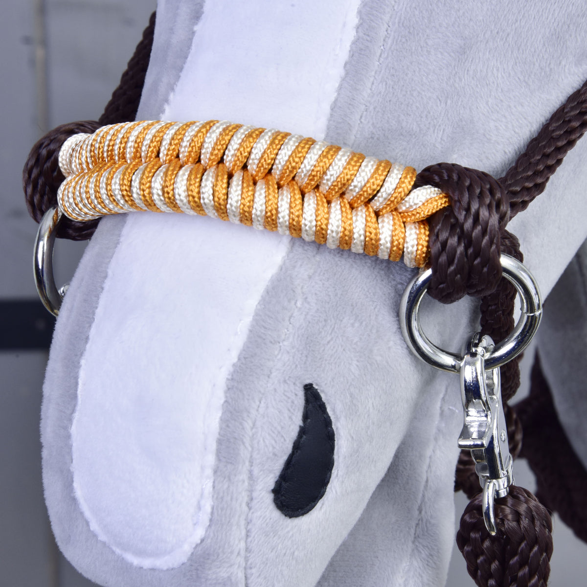 Detail of the orange and white braided noseband and brown rope knot of the Hobby Horse Rope set Orange on a grey head