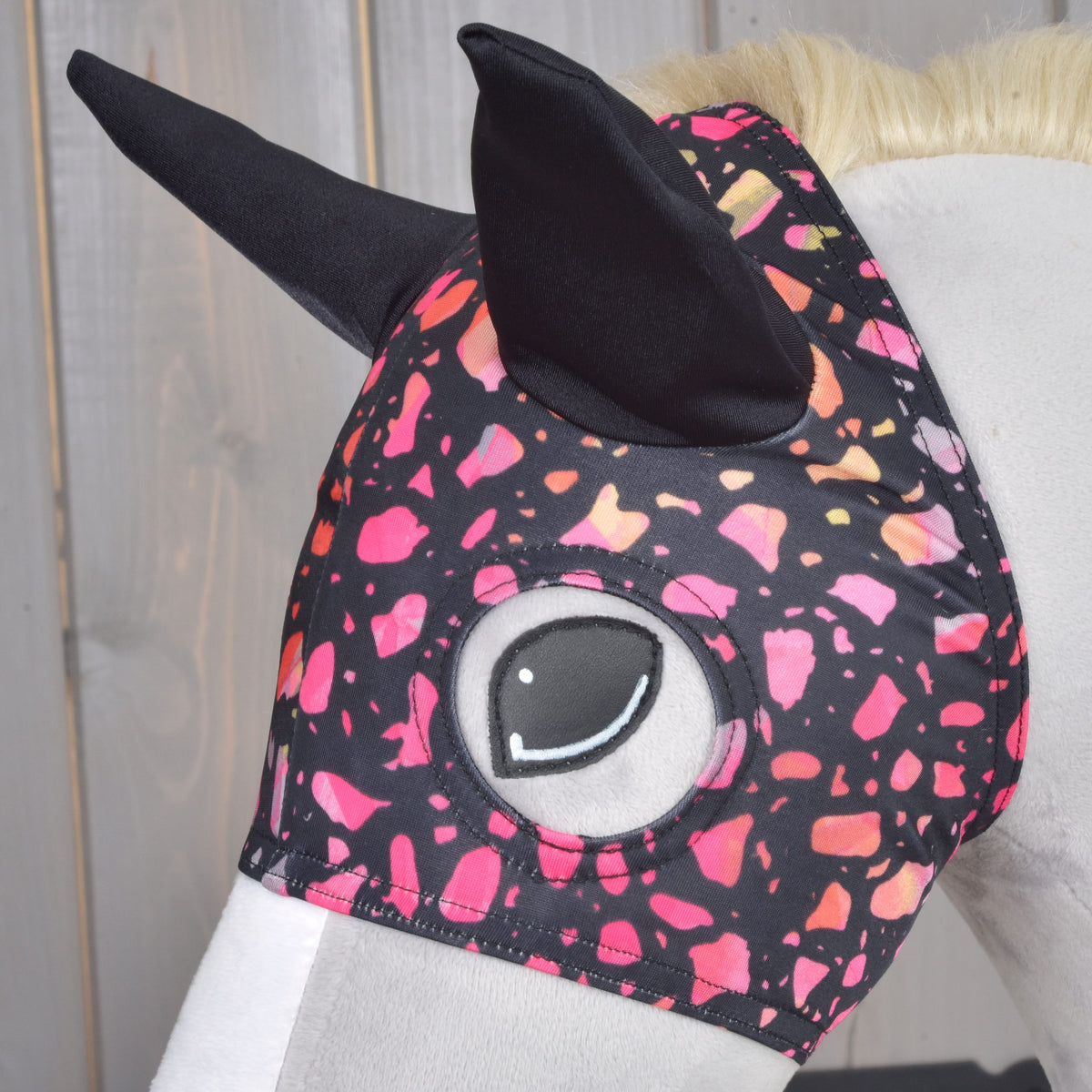 Close-up of the Horse Mask Roxy on a grey Hobby Horse, black ears and the eye opening framed by the pink and coral fleck print