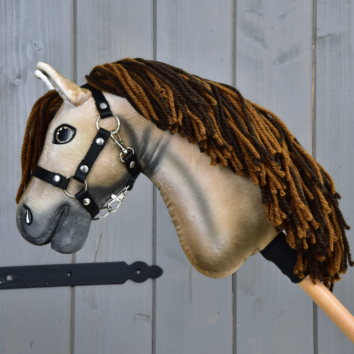Hobby Horse Ruby, en beige mustang, i vänster profil med svart grimma med silverringar på en träkäpp