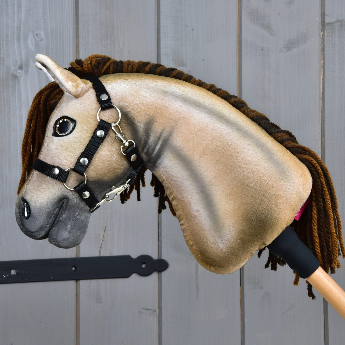 Hobby Horse Ruby från sidan med skuggad beige hals i plysch och brun man av garn mot en grå trädörr