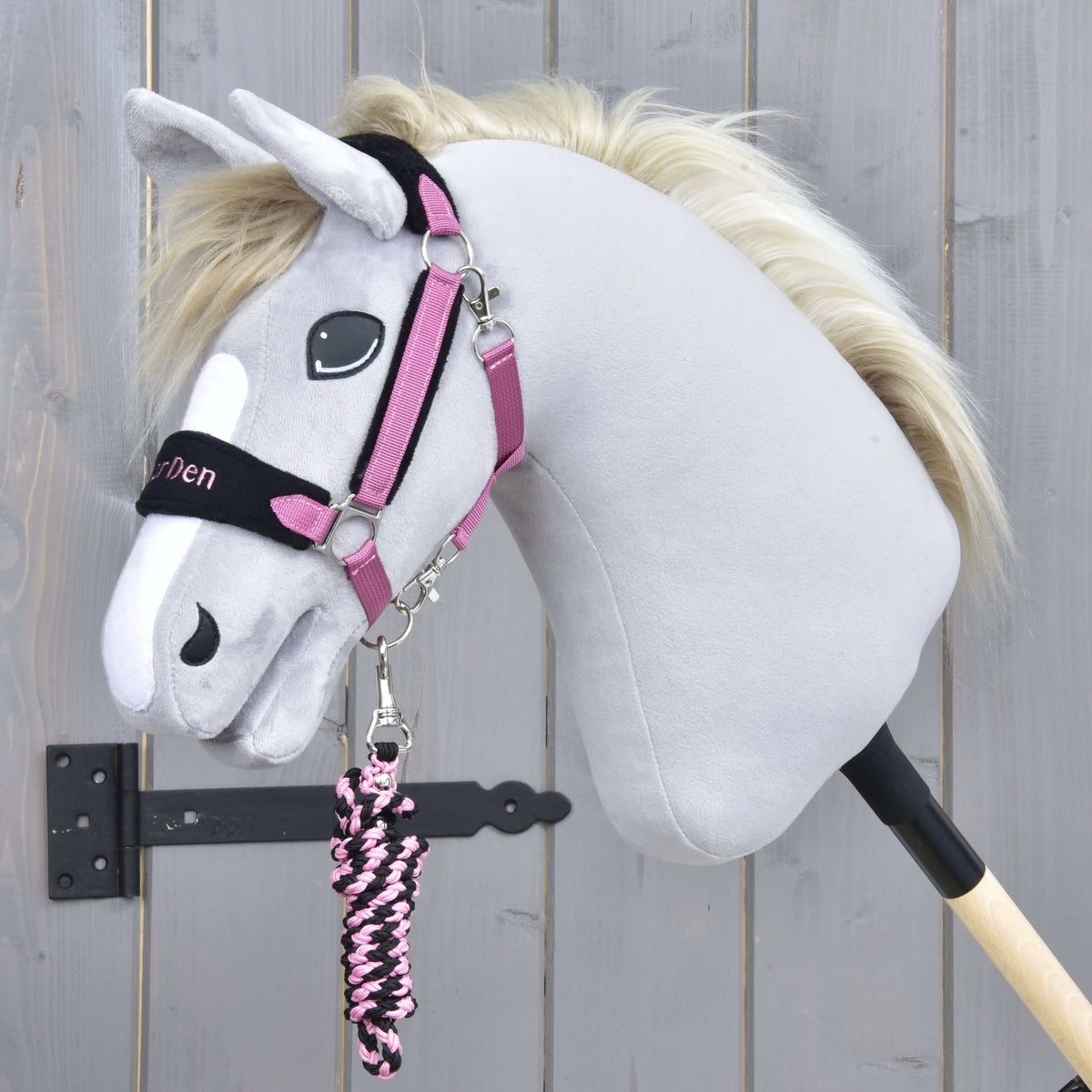 Grimman Exclusive Pink på en grå käpphäst med krämvit man, det rosa och svarta flätade grimskaftet upprullat under hakan