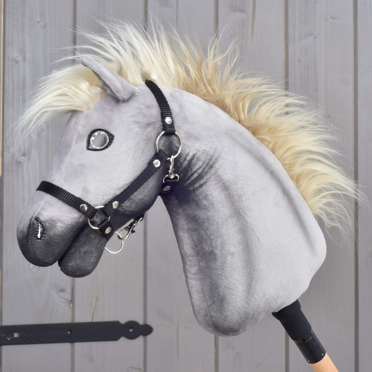 LarDen Hobby Horse Silver Dream with grey plush head, cream mane and black halter, side view by a wooden stable door