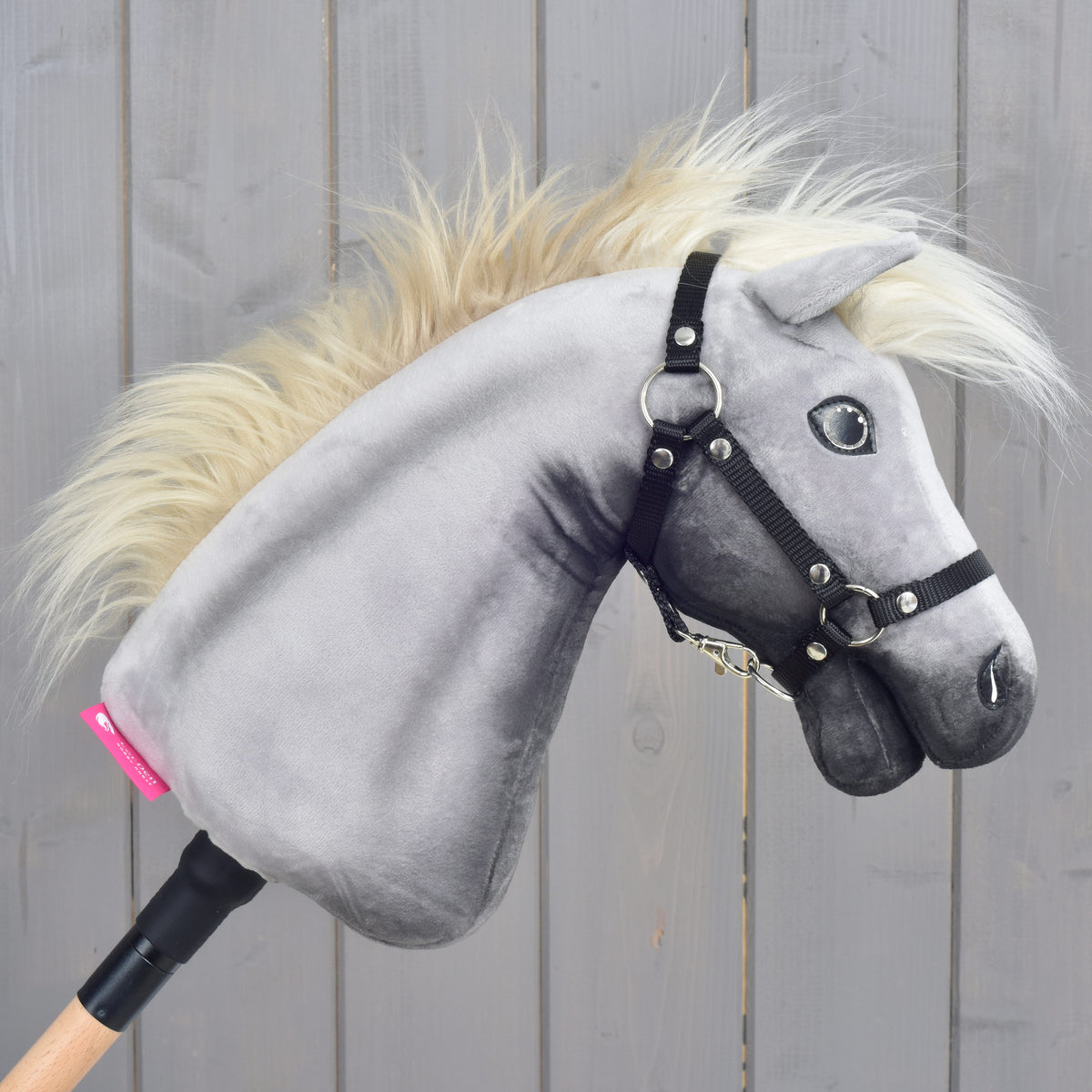 Right profile of the Silver Dream Hobby Horse with grey plush head, black halter and pink label on the wooden stick