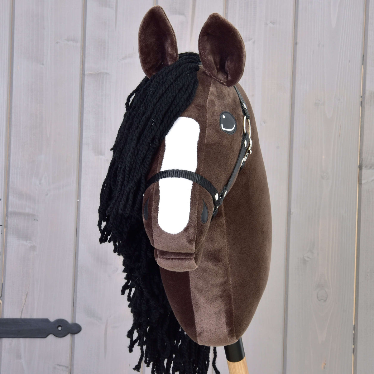 Den mörkbruna Hobby Horse Sisi framifrån med vit bläs, svart pannlugg av garn och svart grimma