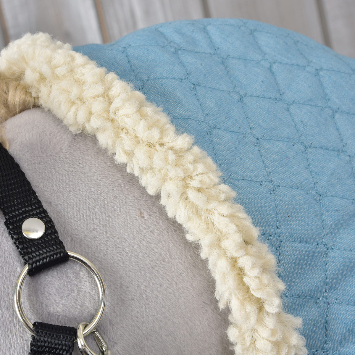 Cream fleece edge of the Stable Blanket Sky Blue curving over a grey Hobby Horse, beside the black halter and silver ring