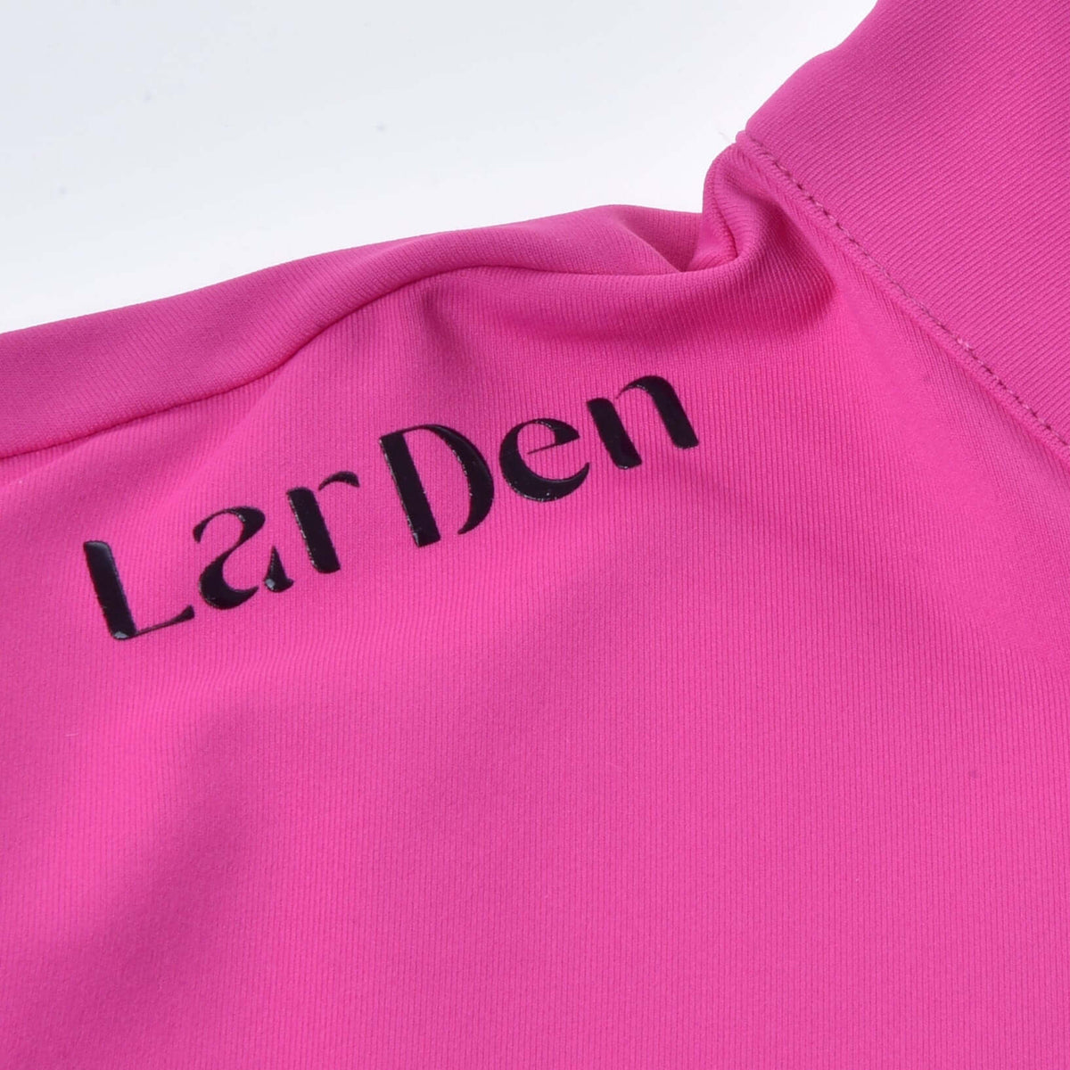 Närbild av svart LarDen-text på axeln av den klarrosa Hobby Horse T-shirten, bredvid kragen
