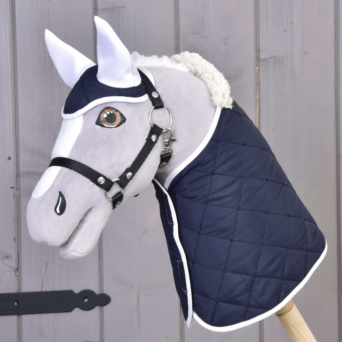 Grey Hobby Horse in a black halter wearing the navy quilted blanket with white trim and matching ear bonnet