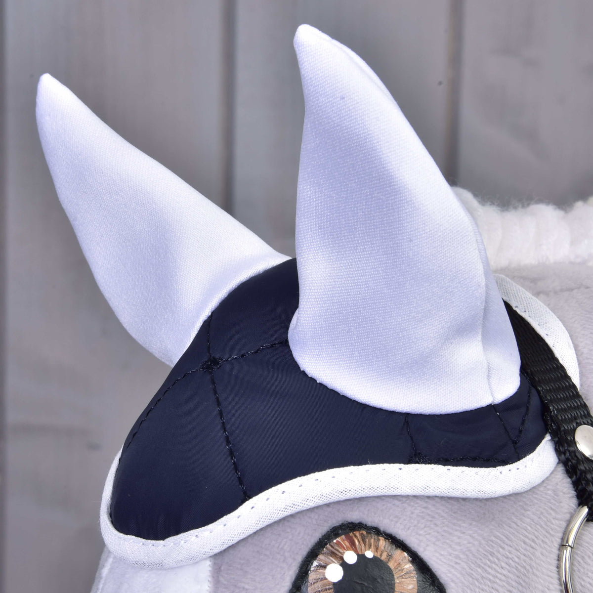 Close-up of the navy quilted ear bonnet with white ear covers and white trim on a grey Hobby Horse