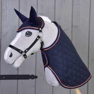 Grey Hobby Horse in a black halter wearing the navy quilted blanket and ear bonnet with orange piping