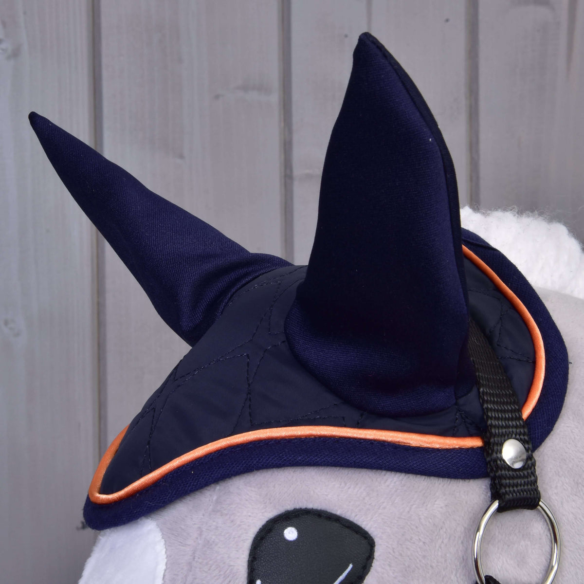 Close-up of the navy ear bonnet with tall navy ears and orange piping on a grey Hobby Horse