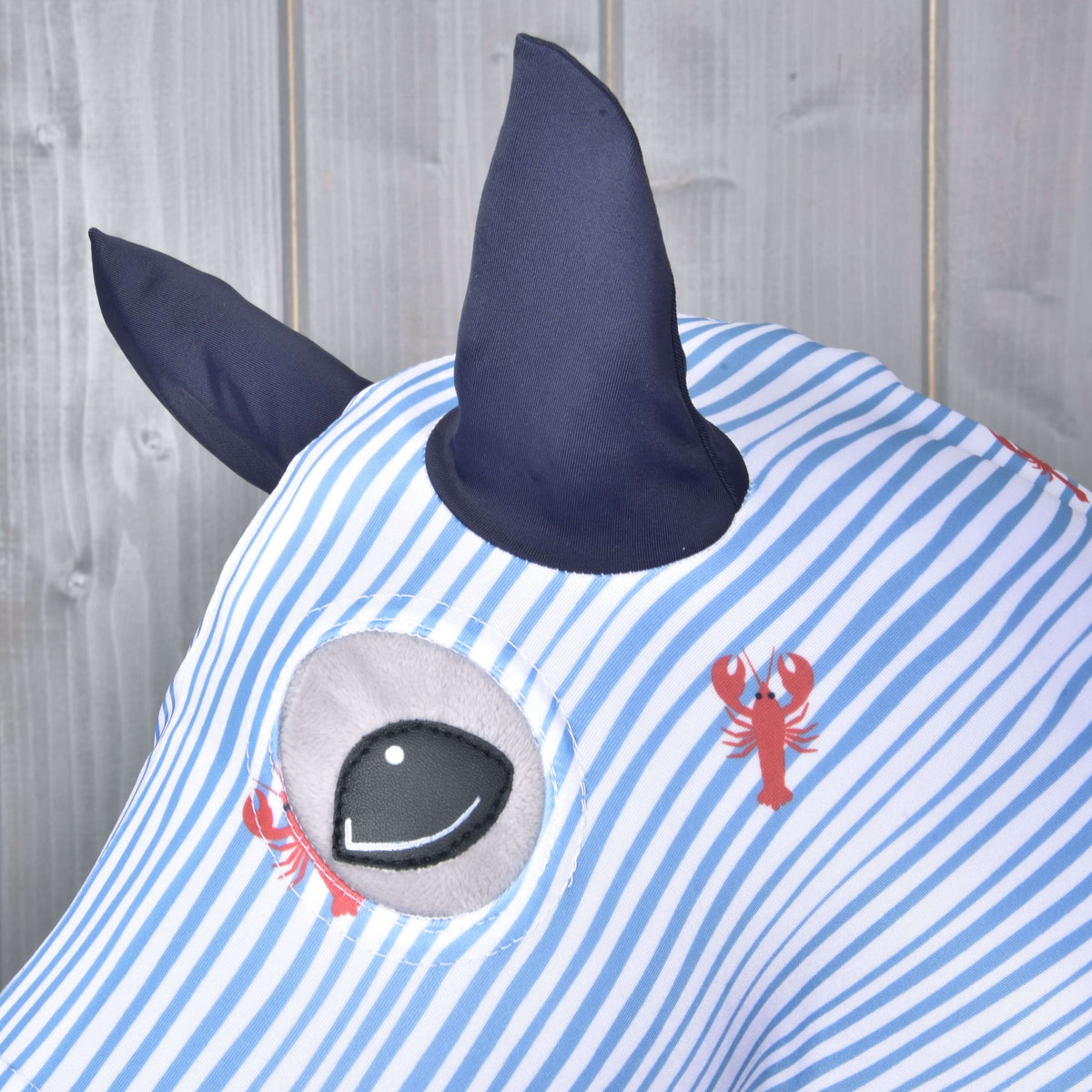 Close-up of the navy ears and eye opening on the blue striped Lycra suit with little red lobsters on a grey Hobby Horse
