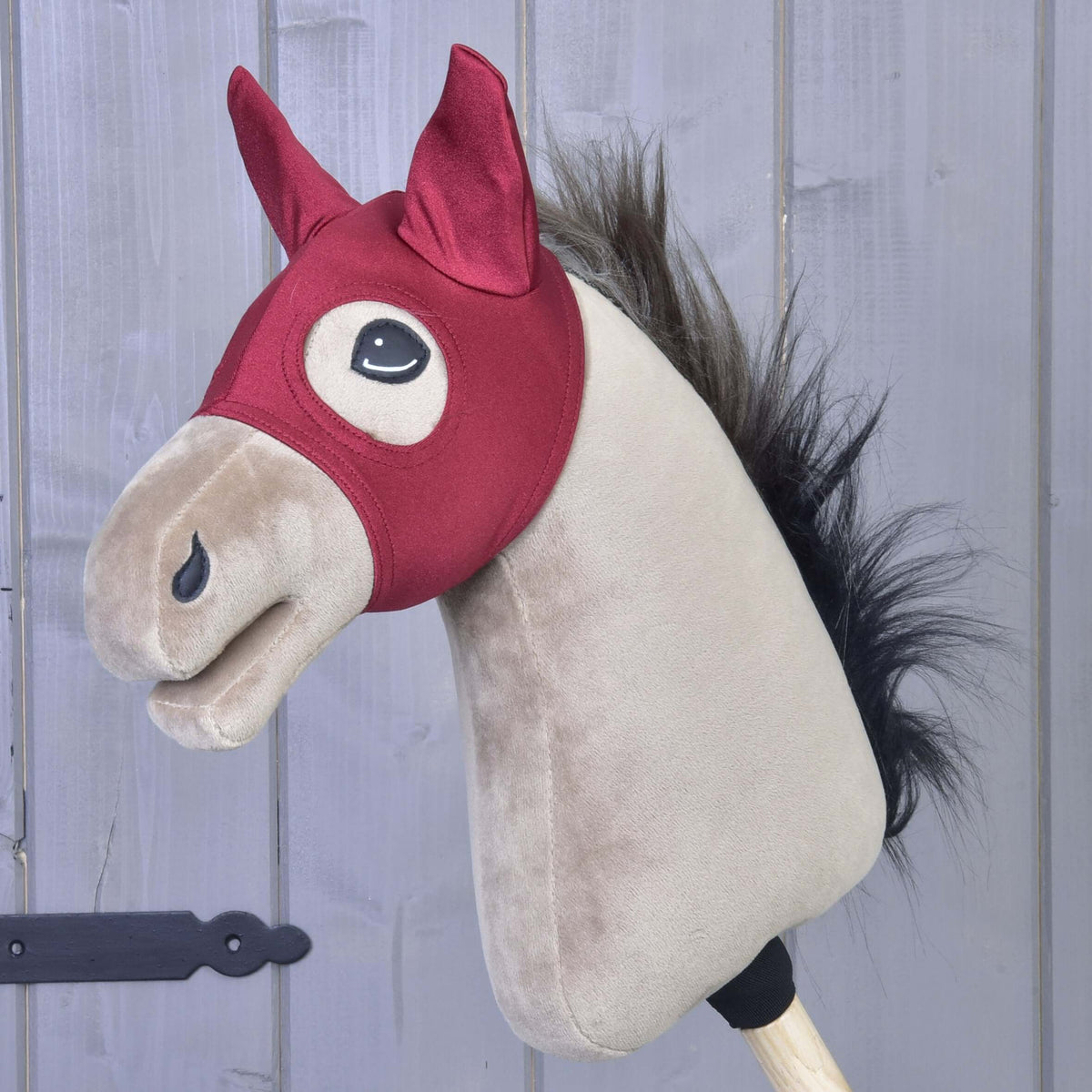 Mask Barn Red från LarDen på en beige käpphäst, mörkrött stretchtyg med spetsiga öronskydd och ögonöppningar