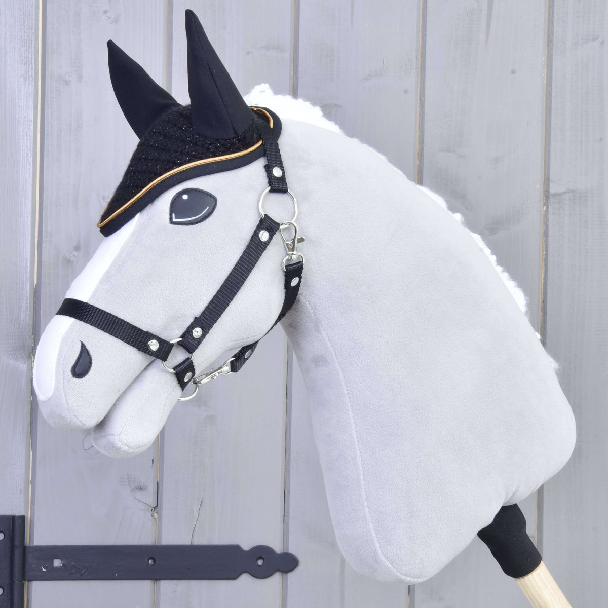Grey Hobby Horse with a black halter and white fur mane wearing the black crocheted ear bonnet with gold trim