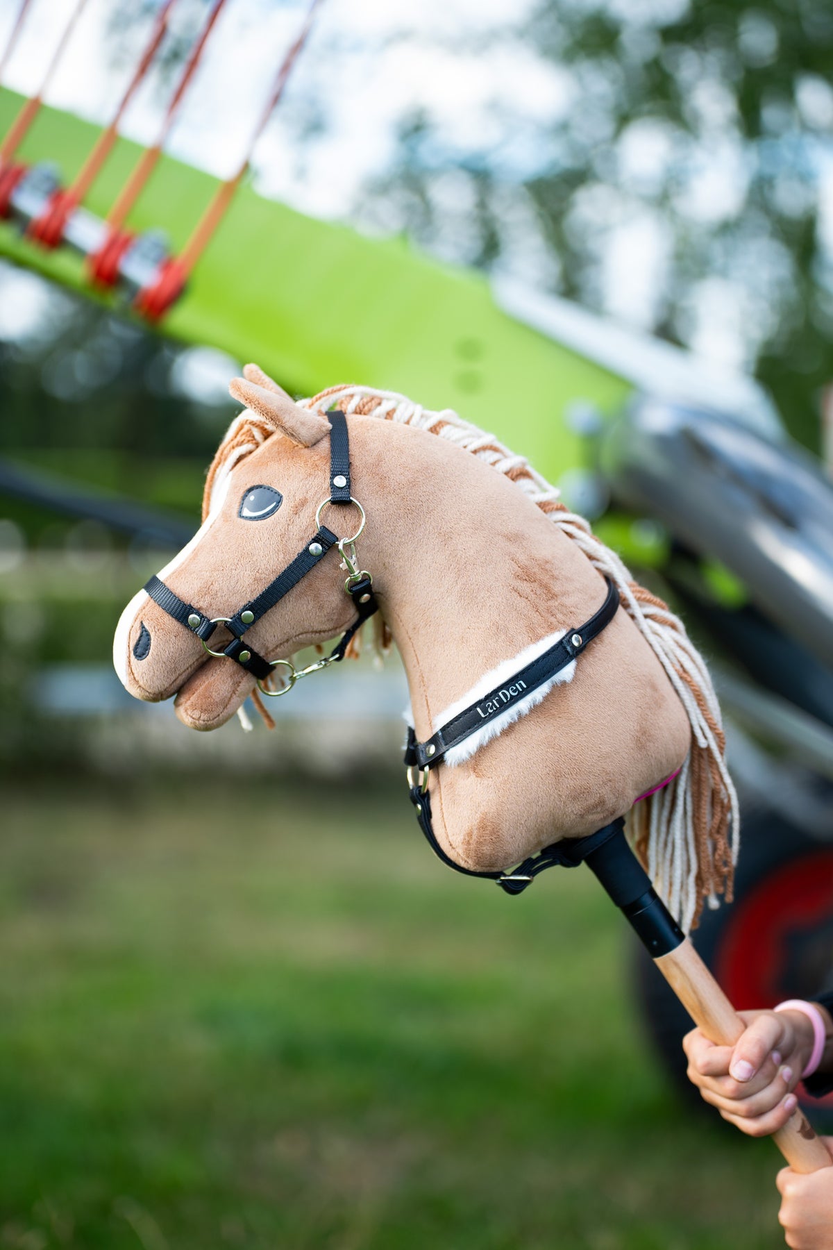 Hobby Horse Bren i svart grimma och svart brösta med vit päls och texten LarDen, en grön lantbruksmaskin bakom