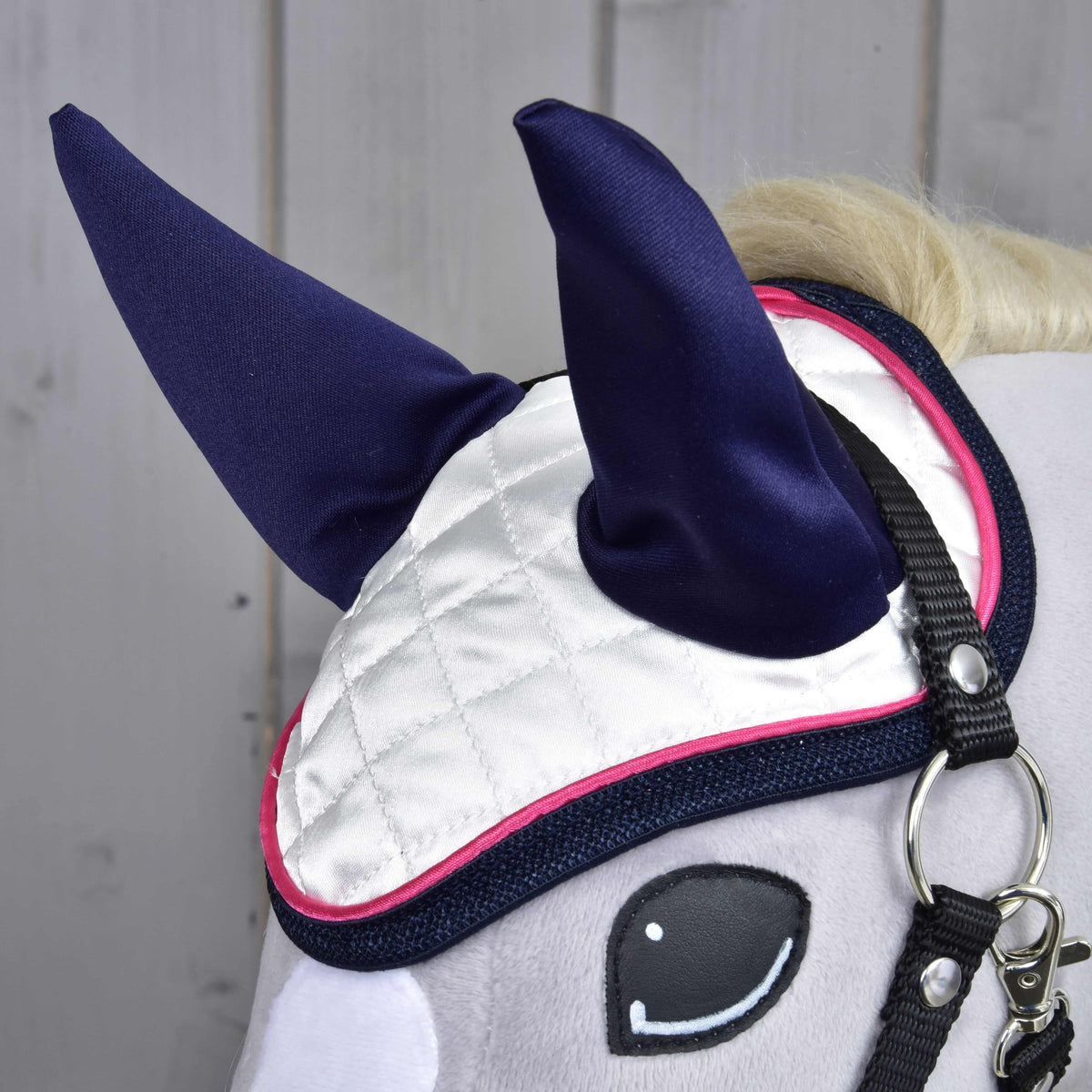 Närbild av den vita quiltade flughuvan i satin med marinblå öronskydd, rosa passpoal och marinblått kantband ovanför ögat
