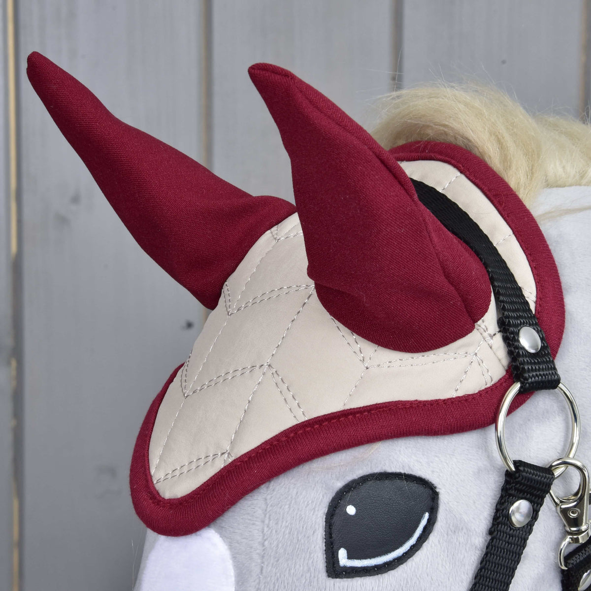 Närbild av flughuvan Maroon Star på en grå käpphäst: vinröda öronskydd och krämvit quiltning med vinrött kantband