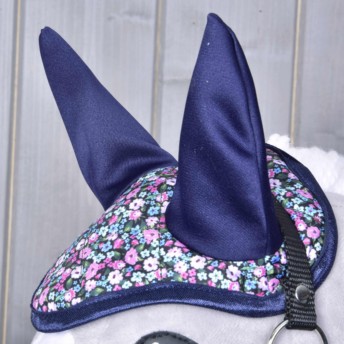 Närbild av de marinblå öronen och den quiltade blommönstrade ovansidan med marinblått kantband på huvudet av en grå käpphäst