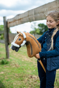 Girl in a navy gilet by a wooden paddock fence holding the golden Hobby Horse in a white fur halter