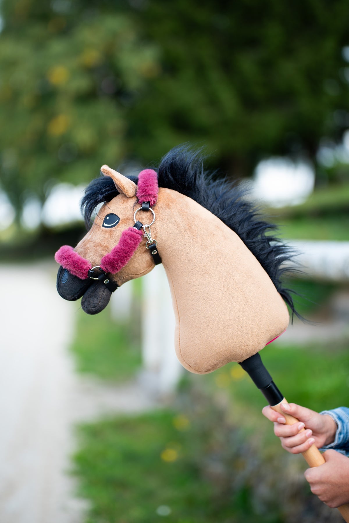 Hobby Horse Cookie in a black halter with raspberry pink fur and a shaggy black mane, held up in front of trees