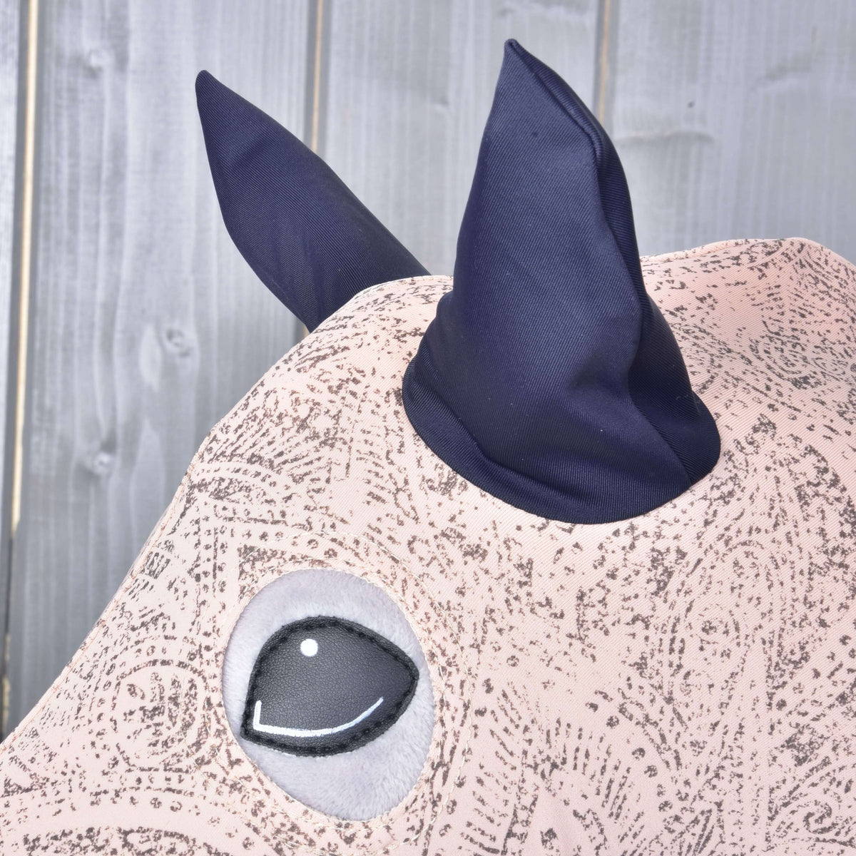 Close-up of the navy ears and round eye opening of the pink paisley Lycra suit on a grey Hobby Horse