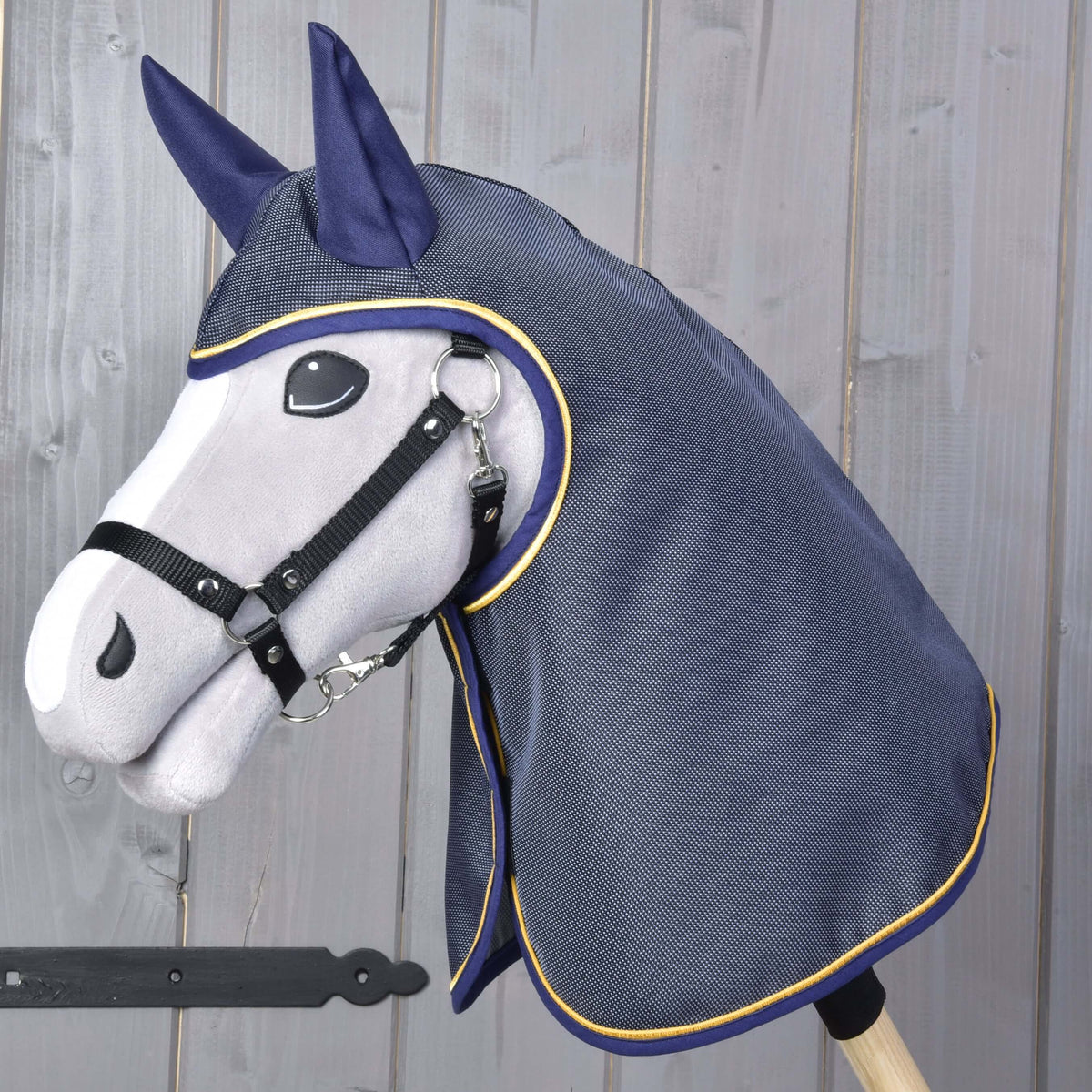 Grey Hobby Horse in a black halter wearing the navy raincoat with ear covers and gold piping over its head and neck