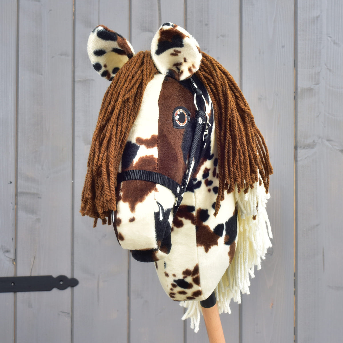 Hobby Horse Dakota med svart grimma framifrån, brun pannlugg av garn och fläckiga öron ovanför bärnstensfärgade ögon