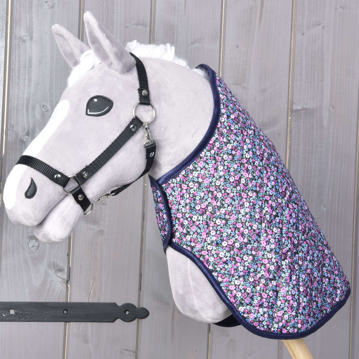 Grey Hobby Horse in a black halter wearing the quilted flower print blanket with navy binding over its neck