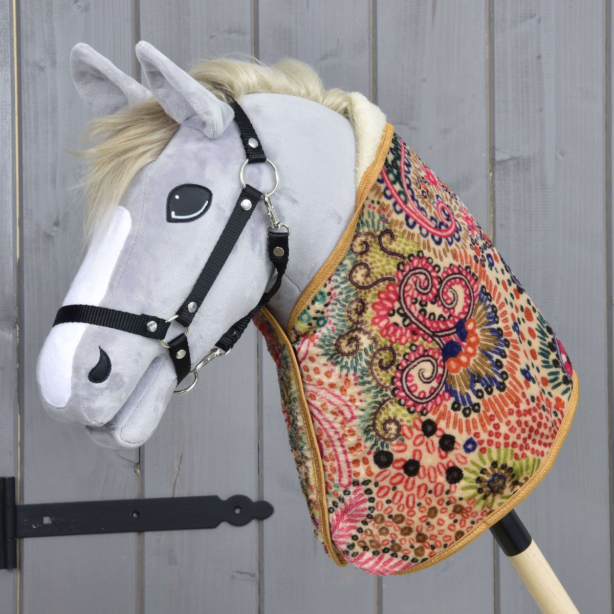 Grey plush Hobby Horse in a black halter wearing the colourful patterned blanket with pink, green and navy swirls
